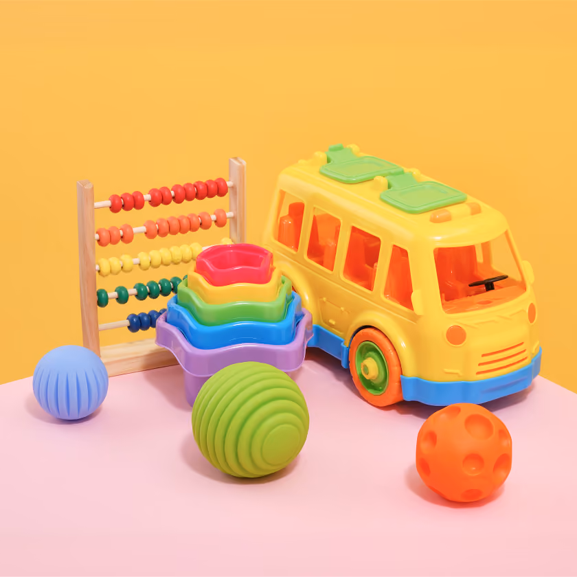 Colorful children's toys including a yellow toy bus, an abacus, stacking cups, and textured balls.